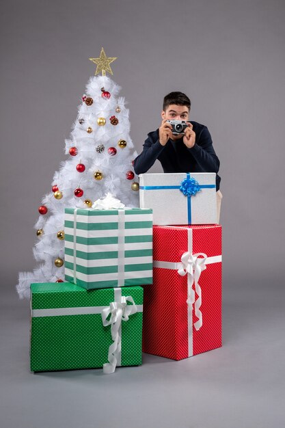 Vorderansicht junger Mann mit Geschenken und Kamera auf dem Grau
