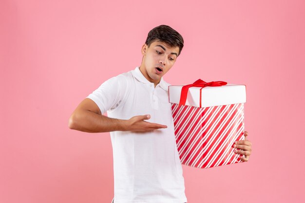 Vorderansicht junger Mann mit großem Weihnachtsgeschenk auf hellrosa Hintergrund