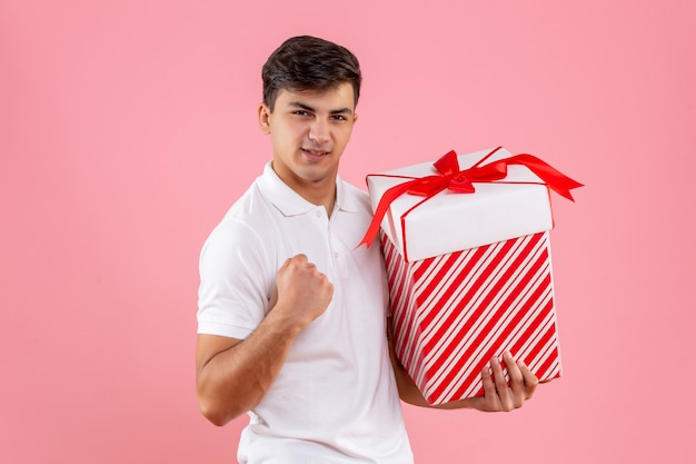 Vorderansicht junger Mann mit großem Weihnachtsgeschenk auf rosa Hintergrund