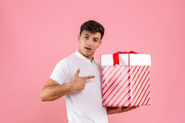 Vorderansicht junger Mann mit großem Weihnachtsgeschenk auf rosa Hintergrund