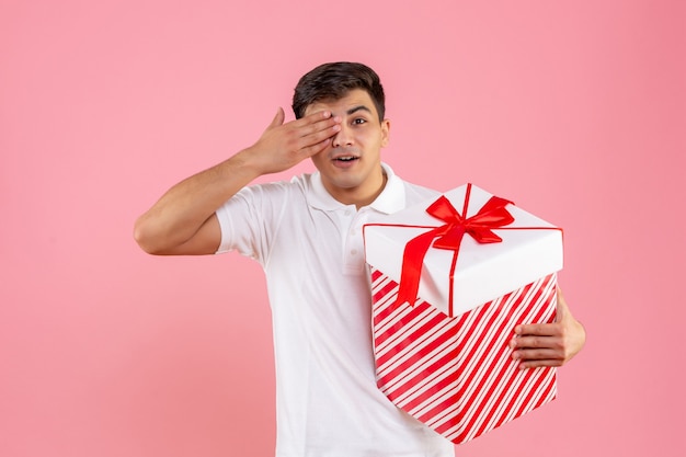 Vorderansicht junger Mann mit großem Weihnachtsgeschenk auf rosa Hintergrund