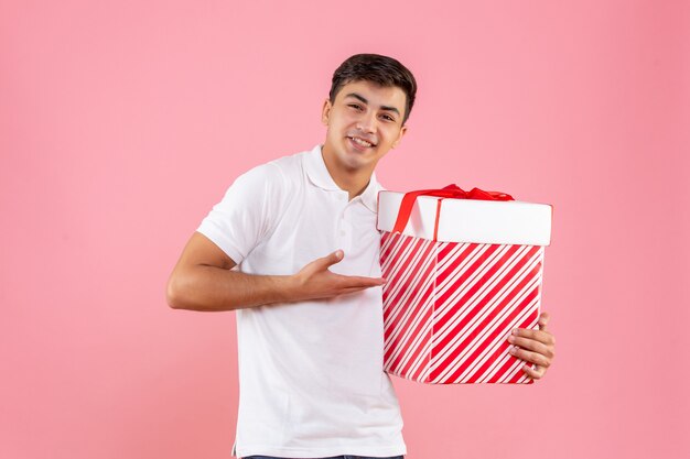 Vorderansicht junger Mann mit großem Weihnachtsgeschenk auf rosa Hintergrund