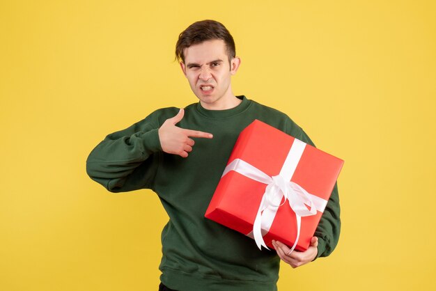 Vorderansicht junger Mann mit grünem Pullover, der auf Geschenk auf Gelb zeigt