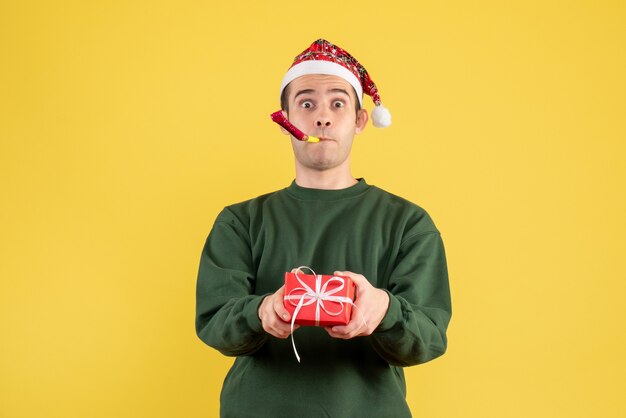 Vorderansicht junger Mann mit grünem Pullover, der Geschenk unter Verwendung des Krachmachers hält auf Gelb hält