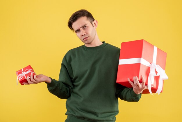 Vorderansicht junger Mann mit grünem Pullover, der seine Geschenke hält, die auf Gelb stehen