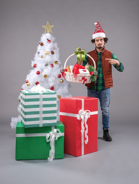 Vorderansicht junger Mann mit Korb um Geschenke auf grauem Schreibtisch Menschen Neujahr Weihnachten