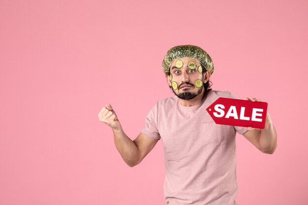 Vorderansicht junger Mann mit Maske auf seinem Gesicht, das Verkaufs-Namensschild auf rosa Hintergrund hält