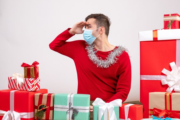 Vorderansicht junger Mann mit Maske, die etwas betrachtet, das um Weihnachtsgeschenke sitzt