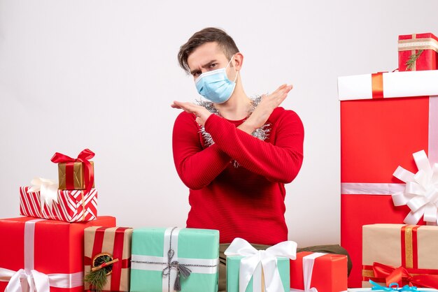 Vorderansicht junger Mann mit Maskenkreuzungshänden, die um Weihnachtsgeschenke sitzen