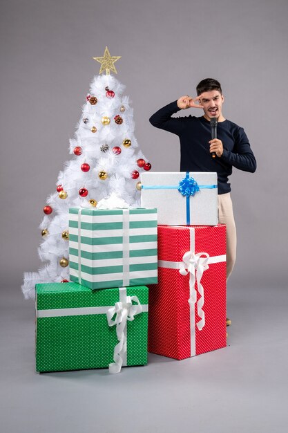 Vorderansicht junger Mann mit Mikrofon mit Geschenken auf dem Grau