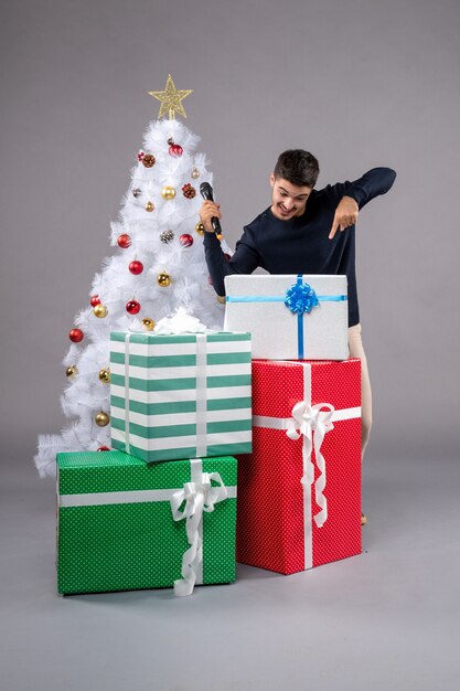 Vorderansicht junger Mann mit Mikrofon und Geschenken auf grauem Schreibtisch Neujahrsgeschenk Weihnachten