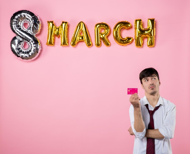 Vorderansicht junger mann mit rosa bankkarte mit marschdekoration auf rosa hintergrund gleichheit farbe geld urlaub shopping mann anwesend party