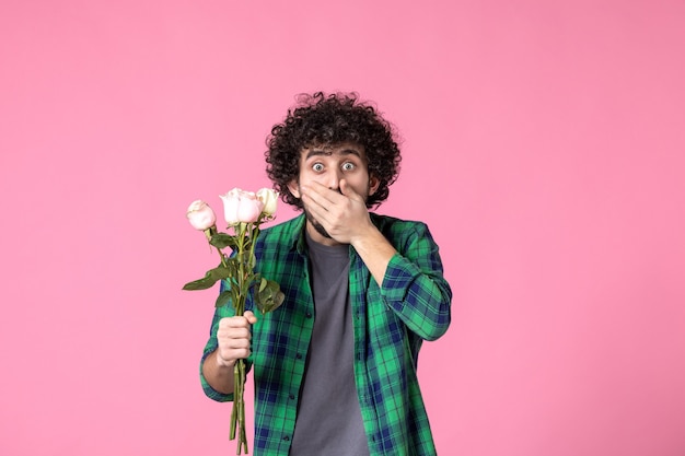 Kostenloses Foto vorderansicht junger mann mit rosa rosen als geschenk zum frauentag auf rosa farbe