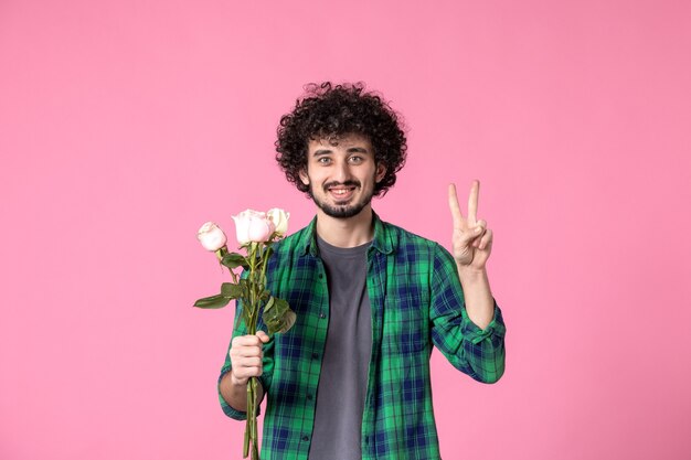 Vorderansicht junger Mann mit rosa Rosen als Geschenk zum Frauentag auf rosa Farbe