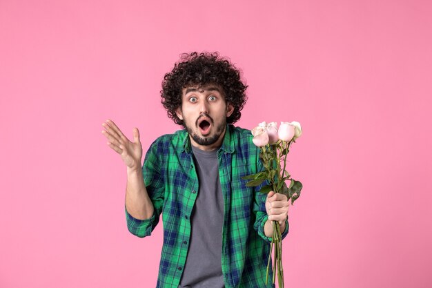 Kostenloses Foto vorderansicht junger mann mit rosa rosen auf rosa colorr