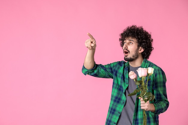 Vorderansicht junger Mann mit rosa Rosen, die auf Rosa in eine Richtung zeigen