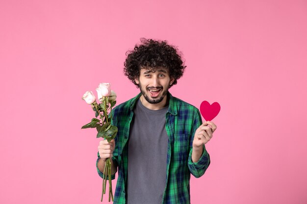 Vorderansicht junger Mann mit rosa Rosen und Herzaufkleber auf rosa