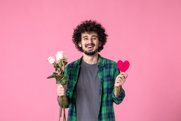 Vorderansicht junger Mann mit rosa Rosen und Herzaufkleber auf rosa