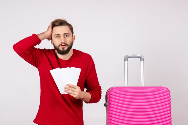 Vorderansicht junger Mann mit rosa Tasche und Halten von Eintrittskarten auf weißer Wandreise Flugfarbreise Urlaubsfoto Emotion