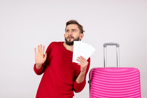 Kostenloses Foto vorderansicht junger mann mit rosa tasche und halten von tickets auf weißen wandreiseflügen farbreise touristenurlaub foto emotion