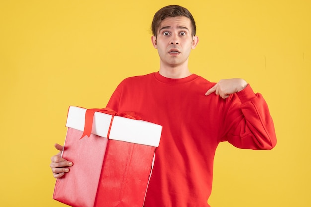 Vorderansicht junger Mann mit rotem Pullover, der auf gelbem Hintergrund steht
