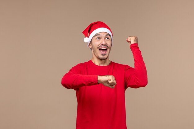 Vorderansicht junger Mann mit rotem Weihnachtsumhang auf braunem Boden Emotion Weihnachtsferien