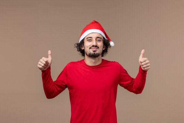 Vorderansicht junger Mann mit rotem Weihnachtsumhang auf braunem Hintergrundweihnachtsgefühlfeiertag