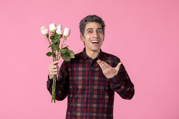 Vorderansicht junger Mann mit schönen rosa Rosen auf rosa Wand