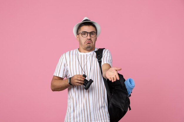 Vorderansicht junger Mann mit Tasche und Fernglas auf dem rosa Hintergrund