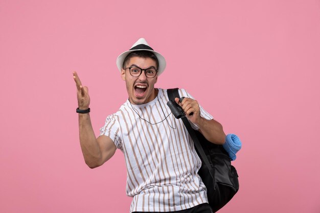 Vorderansicht junger Mann mit Tasche und Fernglas auf dem rosa Hintergrund