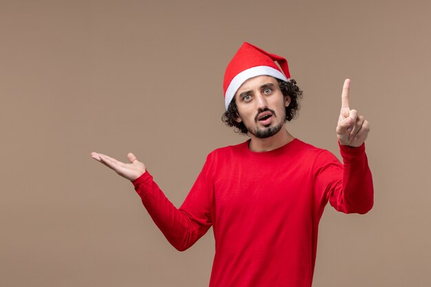 Vorderansicht junger Mann mit überraschtem Ausdruck auf braunem Hintergrundfeiertagsgefühle Weihnachten