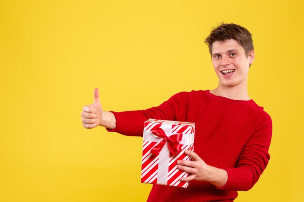 Vorderansicht junger Mann mit Weihnachten Geschenk auf gelbem Boden Geschenk Neujahr menschliche Emotion Farbe Weihnachten