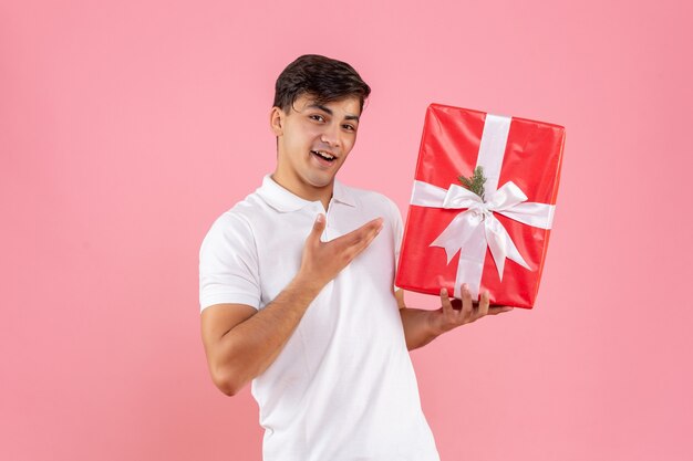 Vorderansicht junger Mann mit Weihnachtsgeschenk auf rosa Hintergrund