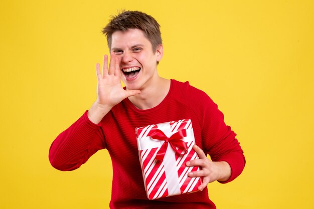 Vorderansicht junger Mann mit Weihnachtsgeschenk, das gelben Hintergrund anruft