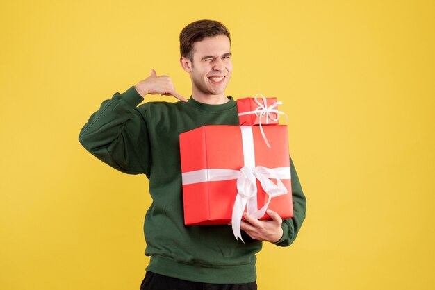 Vorderansicht junger Mann mit Weihnachtsgeschenk machen rufen mich Telefonzeichen stehend auf gelbem Hintergrund
