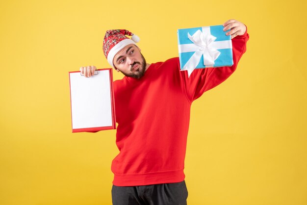 Vorderansicht junger Mann mit Weihnachtsgeschenk und Hinweis auf gelbem Hintergrund