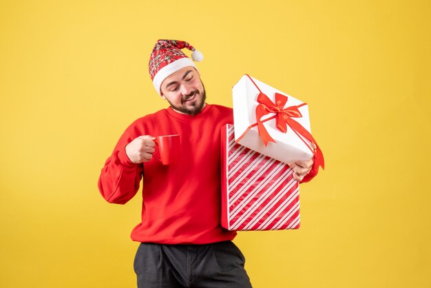 Vorderansicht junger Mann mit Weihnachtsgeschenk und Tasse Tee auf gelbem Hintergrund