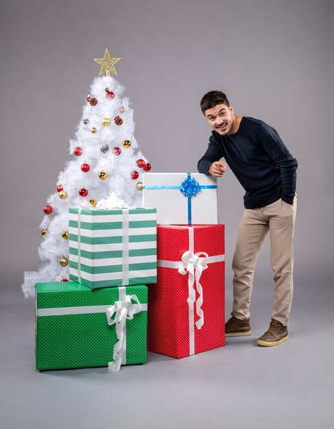 Vorderansicht junger Mann mit Weihnachtsgeschenken auf dem Grau