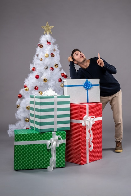 Vorderansicht junger Mann mit Weihnachtsgeschenken auf dem Grau