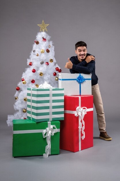 Kostenloses Foto vorderansicht junger mann mit weihnachtsgeschenken auf dem grau