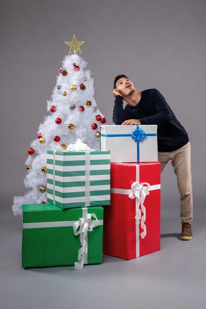 Vorderansicht junger Mann mit Weihnachtsgeschenken auf dem Grau