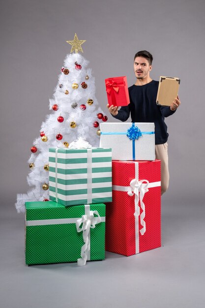 Vorderansicht junger Mann mit Weihnachtsgeschenken auf dem Grau