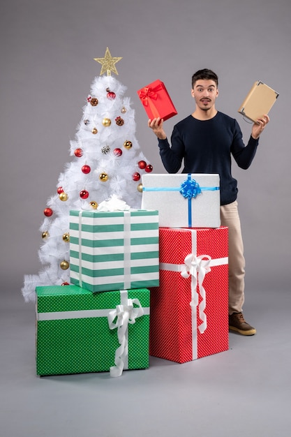 Kostenloses Foto vorderansicht junger mann mit weihnachtsgeschenken auf dem grau