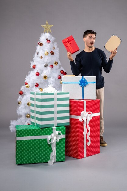 Vorderansicht junger Mann mit Weihnachtsgeschenken auf dem Grau