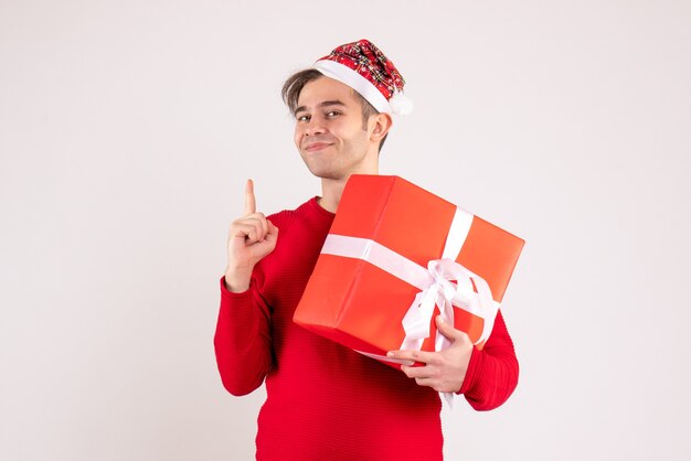 Vorderansicht junger Mann mit Weihnachtsmütze, der Finger oben auf weißem Hintergrund zeigt