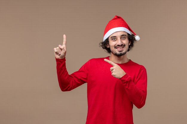 Vorderansicht junger Mann mit Weihnachtsumhang auf dem braunen Hintergrundgefühlfeiertagsweihnachten