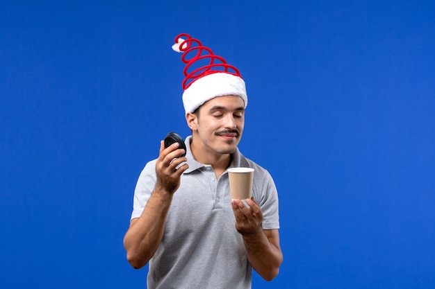 Vorderansicht junger Mann riechender Kaffee auf blauer Wand Neujahrsfeiertagsemotion des Mannes