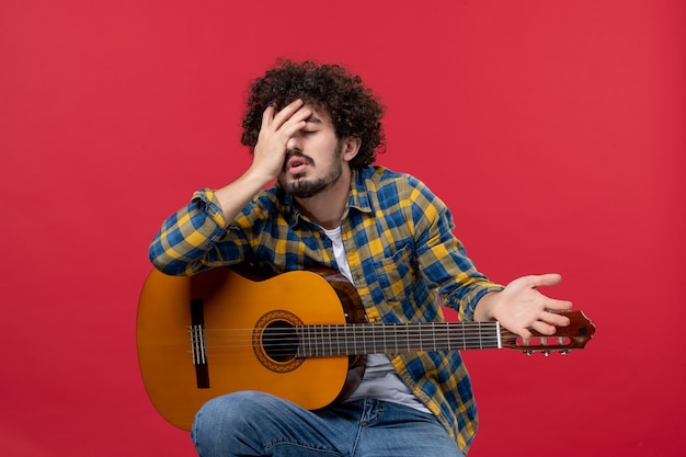 Vorderansicht junger Mann sitzt mit Gitarre auf der roten Wand Musik Performance Musiker Farbapplaus spielen Live-Konzert