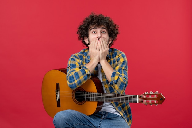 Vorderansicht junger Mann sitzt mit Gitarre auf roter Wand Applaus Band Musiker spielen Musik Farbe live