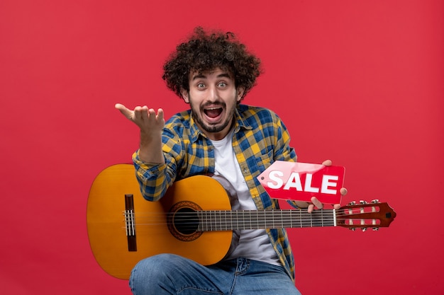 Vorderansicht junger Mann sitzt mit Gitarre auf roter Wand Konzert Live-Musiker Verkauf spielen Musik Farbapplaus